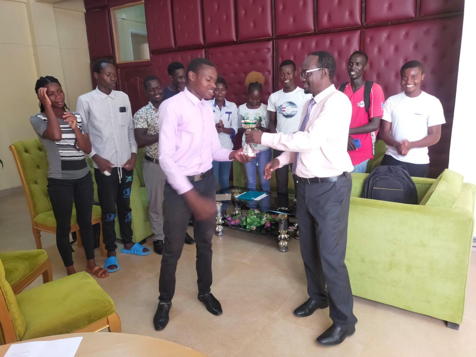 The team leader (job Simiyu) presenting the trophy to the Principal (Prof. George Cheminingw’a)